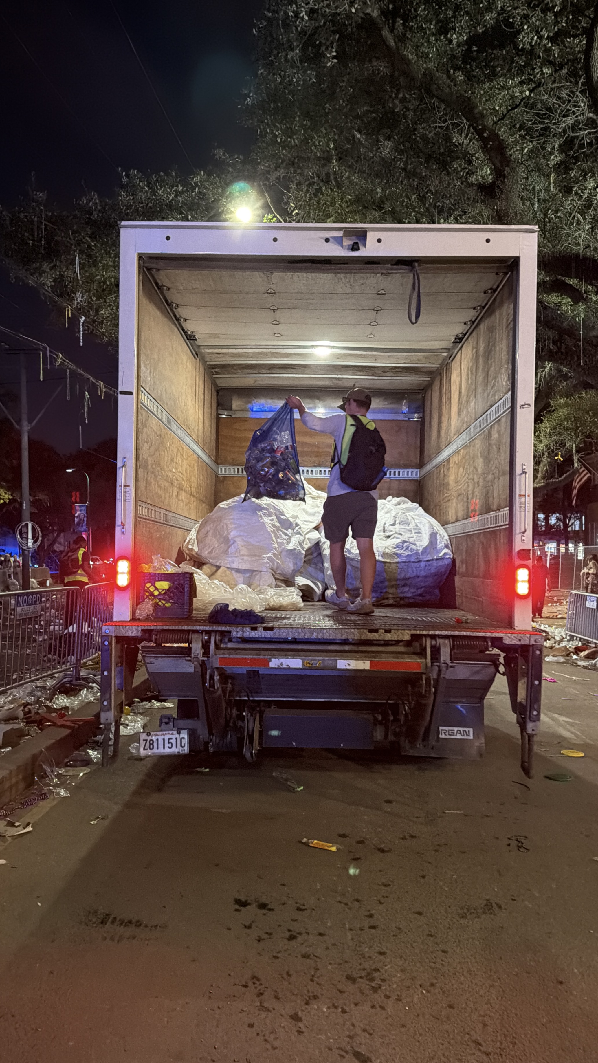 Volunteer loading collected recyclables into a box truck after a Mardi Gras parade