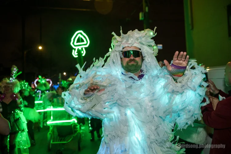 Three krewe members taking a selfie in the middle of the parade, big grins, party lights behind